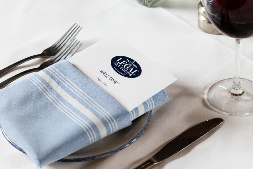 A neatly set dining table features a white plate with a blue-striped napkin, holding a folded menu. The menu has the 